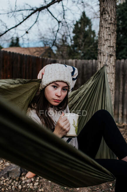 Вертикальний портрет дівчини-підлітка, що розслабляється в гамаку з кавовим чашкою — стокове фото