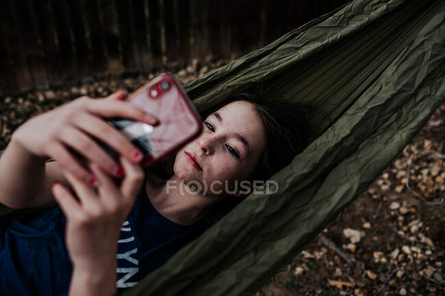 Дівчина лежить в гамаку, граючи на мобільному телефоні — стокове фото