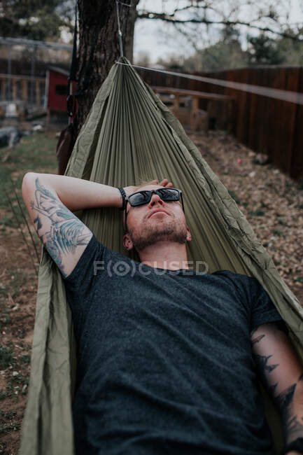 Man in sunglasses relaxing on hammock in backyard — Stock Photo