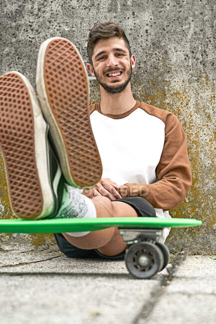 Junger lässiger Mann sitzt auf Skateboard — Stockfoto