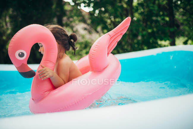 Счастливый ребенок играет в бассейне с водяной игрушкой фламинго — стоковое фото