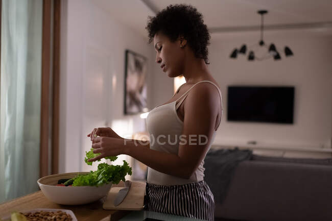 Vista laterale della lattuga lacerazione femminile nera per insalata mentre si cucina una cena sana — Foto stock
