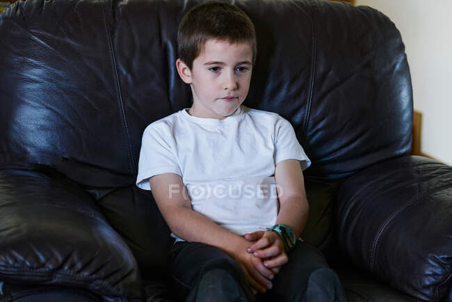 Ребенок сидит на темном диване и смотрит телевизор — стоковое фото