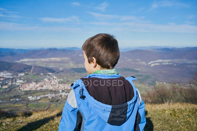 Junge auf dem Rücken blickt mit blauem Mantel auf die herbstliche Landschaft — Stockfoto