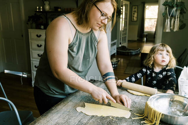 A mother cutting up pasta dough to make noodles — Stock Photo