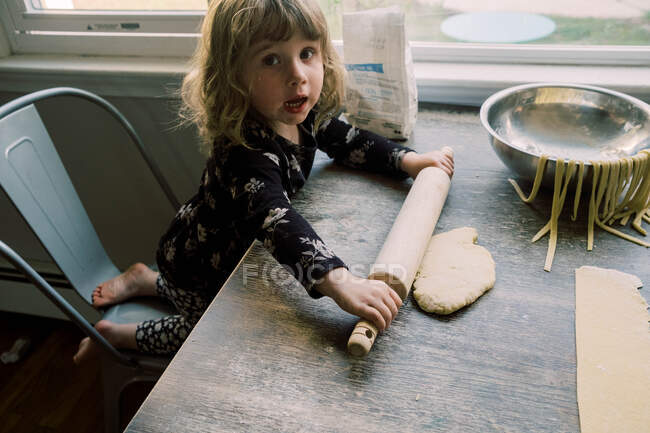 Маленькая девочка, катящая тесто для макарон на стол — стоковое фото