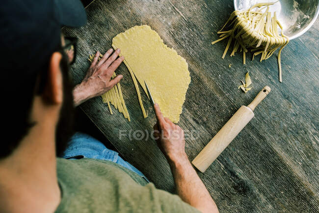 Мужчина режет тесто для макарон, чтобы сделать лапшу — стоковое фото