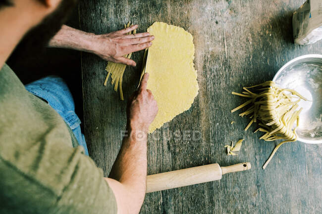 A man cutting up pasta dough to make noodles — Stock Photo