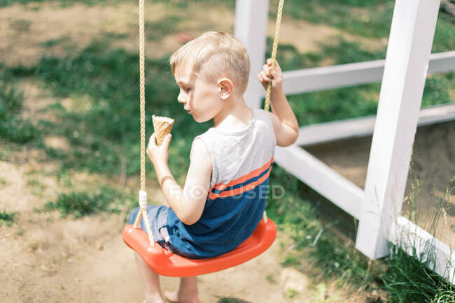 Um menino balançando com seu cone de sorvete na mão — Fotografia de Stock