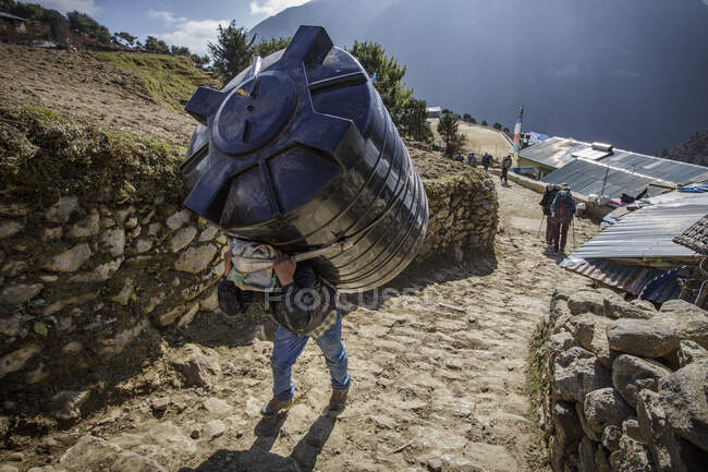 Um trabalhador carrega um tanque de água em seu banco em Namche Bazaar, Nepal. — Fotografia de Stock