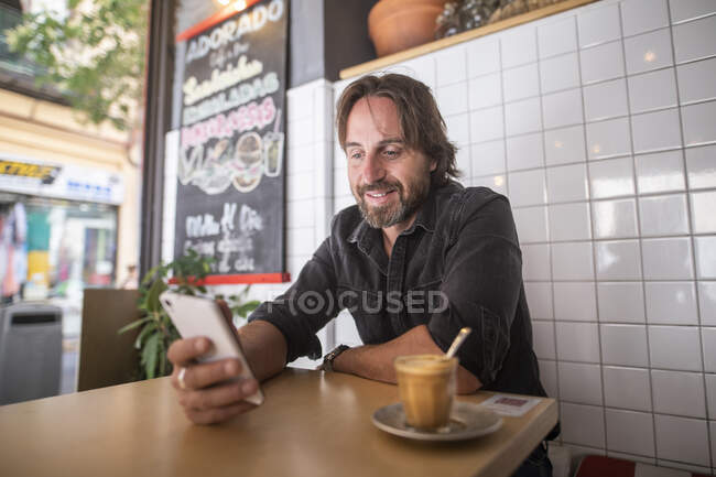 Uomo godendo in una caffetteria guardando il telefono cellulare — Foto stock