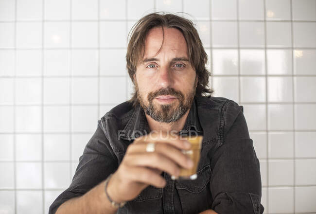 Портрет молодого чоловіка, який п'є каву з старовинною стіною позаду нього — стокове фото
