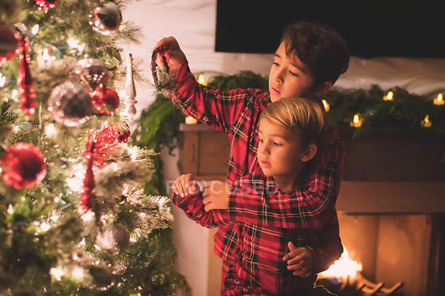 Dois irmãos pendurando ornamentos na Árvore de Natal à noite — Fotografia de Stock