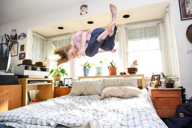 Adolescente pulando na cama pego no ar e sorrindo no quarto ensolarado — Fotografia de Stock