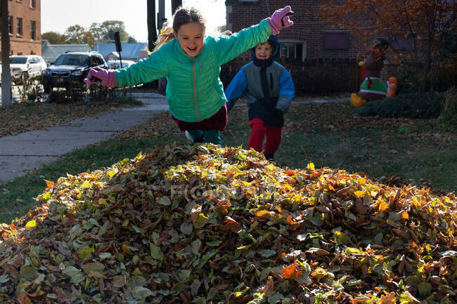 Happy kids jumping into a pile of leaves on a cold fall day — Stock Photo
