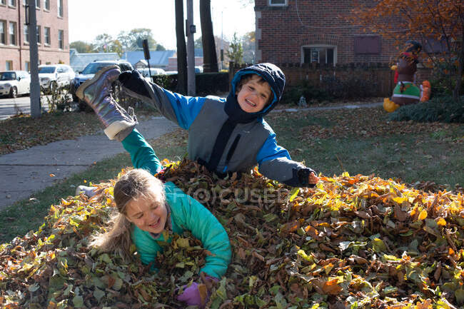 Щасливі брати і сестри стрибають в купу листя в холодний осінній день — стокове фото