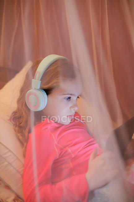 Una joven aprendiendo delante de una tableta mientras está acostada en la cama - foto de stock