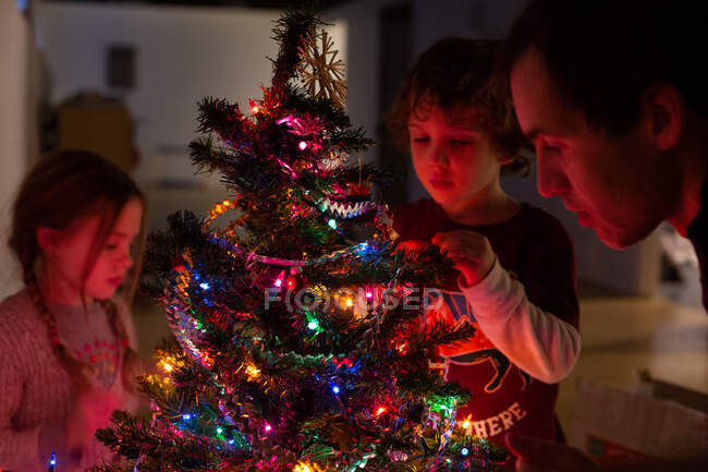 Eine junge Familie schmückt nachts ihren Weihnachtsbaum — Stockfoto