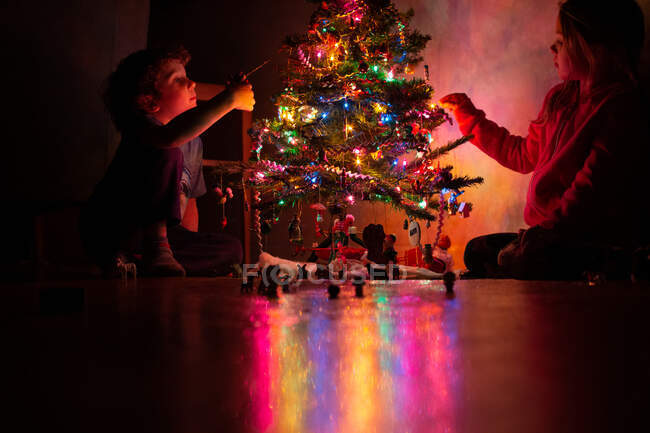 Niños pequeños decorando su árbol de Navidad por la noche - foto de stock