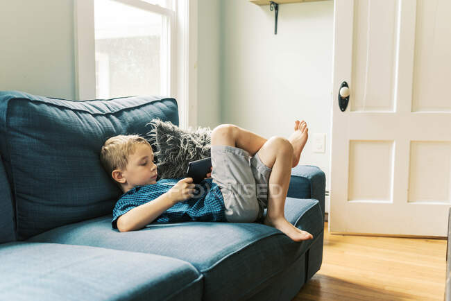 Маленький мальчик с помощью планшетного компьютера на диване дома — стоковое фото