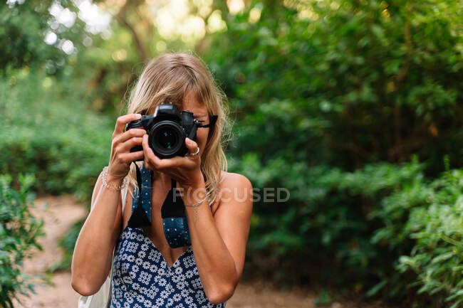 Blonde Frau in blauem Kleid und weißer Stofftasche beim Fotografieren in einem Park. Park des Labyrinths in Barcelona — Stockfoto