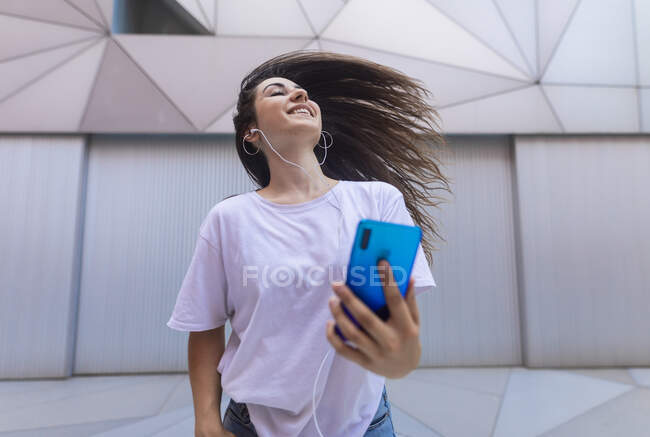 Young woman dancing on the street with headphones while moving her hair — Stock Photo