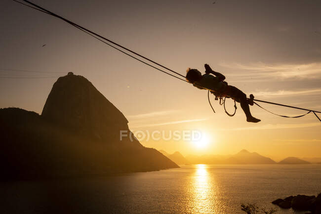 Beautiful sunrise view of man walking on highline with Sugar Loaf Mountain and ocean on the back, Rio de Janeiro, Brazil — Stock Photo