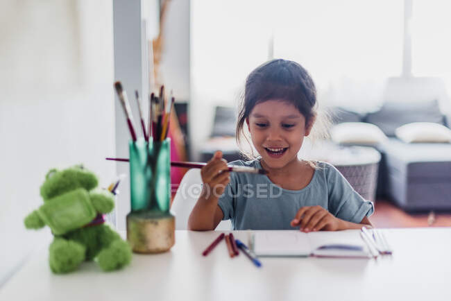 Spanisches Mädchen malt mit Bleistiften und Farben auf dem Schreibtisch. — Stockfoto