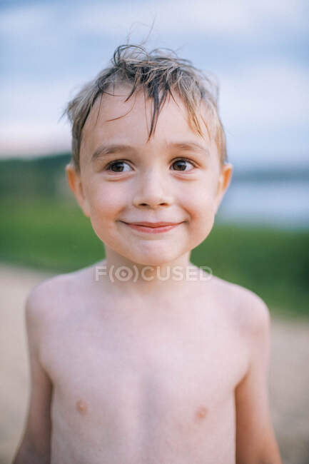 A sweet five year old boy on the beach, smiling shyly — Stock Photo