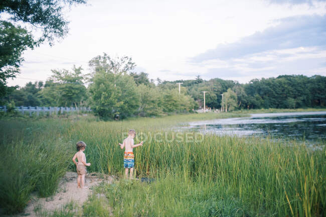Dos niños empapados de pie en las hierbas altas junto a un lago - foto de stock