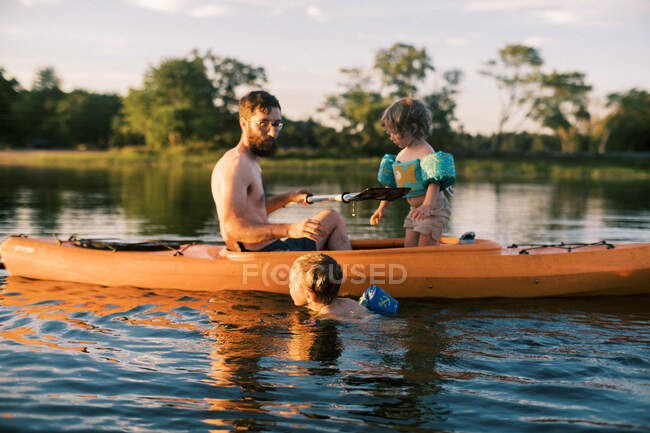 Eine junge Familie paddelt und schwimmt bei Sonnenuntergang an einem See — Stockfoto