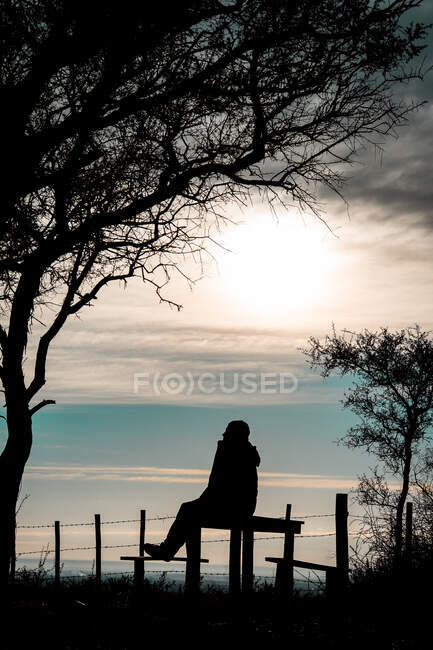 Silhouette eines Mannes, der bei Sonnenaufgang auf einer Bank sitzt — Stockfoto