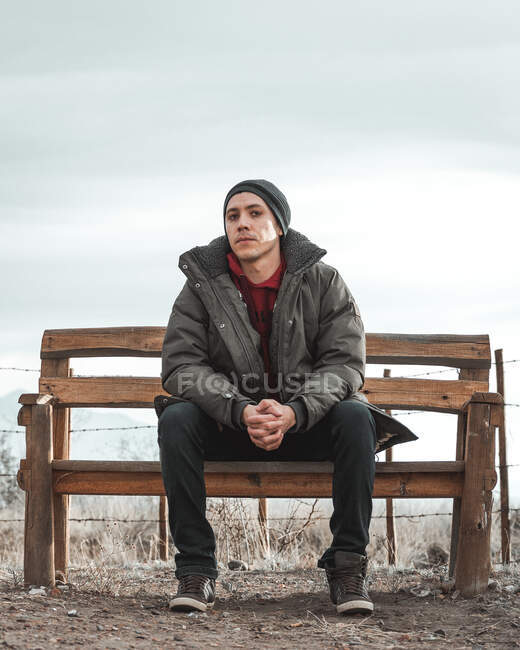 Молодой человек сидит на скамейке со сжатыми руками — стоковое фото