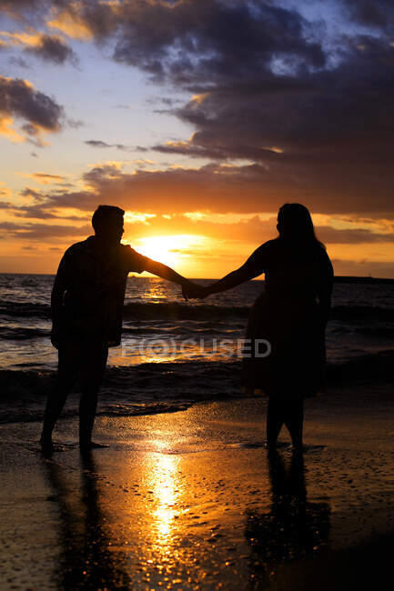 Um jovem casal caminhando na praia ao pôr do sol — Fotografia de Stock