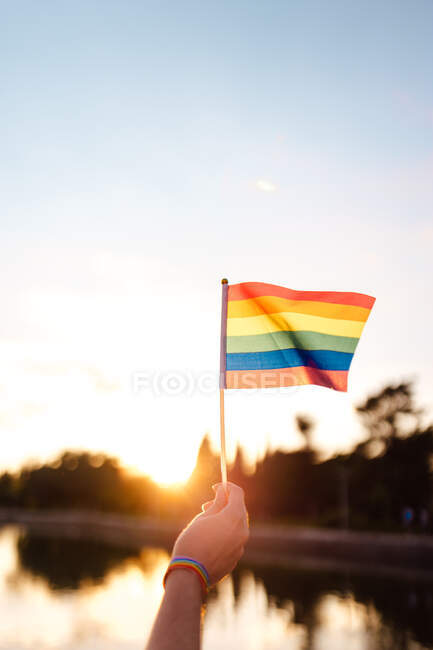 Woman hand with rainbow ribbon wristband holding lgbt flag at sunset — Stock Photo