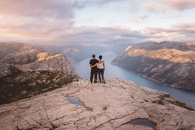 Пара стоїть на скелі в Преікестолен, Норвегія під час заходу сонця. — стокове фото