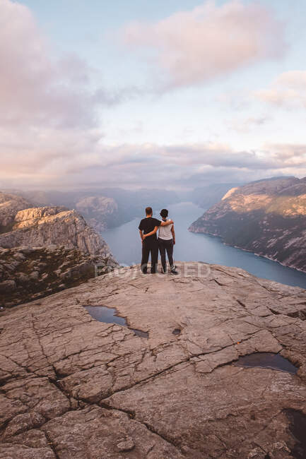 Casal em pé no penhasco em Preikestolen, Noruega durante o pôr do sol — Fotografia de Stock