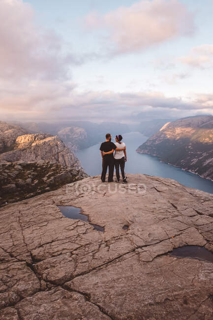 Пара стоящих лицом друг к другу на скале в Прейкстолене, Норвегия на закате — стоковое фото