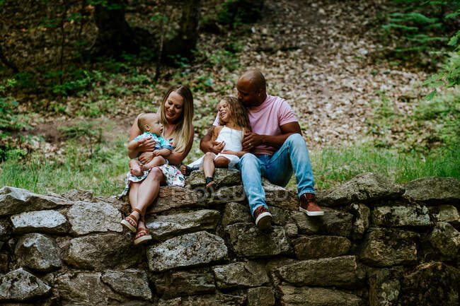 Glückliche junge vielseitige Familie sitzt lächelnd auf Felsen im Wald — Stockfoto