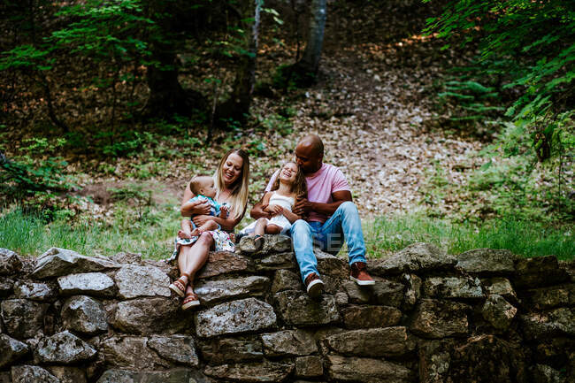 Щаслива багаторасова сім'я сміється, сидячи на каменях у лісі — стокове фото