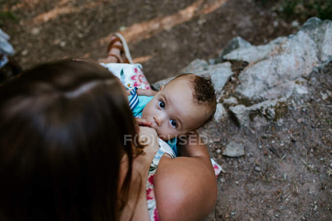 Niño mirando hacia arriba mientras amamanta con su mamá - foto de stock