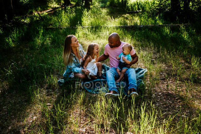 Joven familia riendo y riéndose mientras se sienta en el suelo afuera - foto de stock