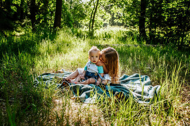 Sister kissing infant brother outside in tall grass — Stock Photo