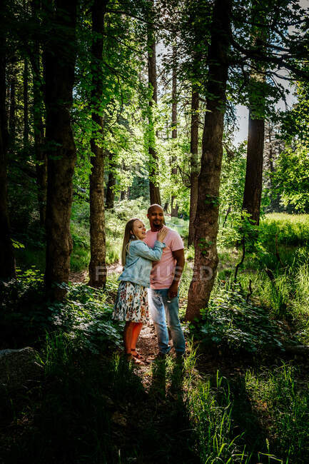 Biracial casal de pé e rindo na floresta — Fotografia de Stock