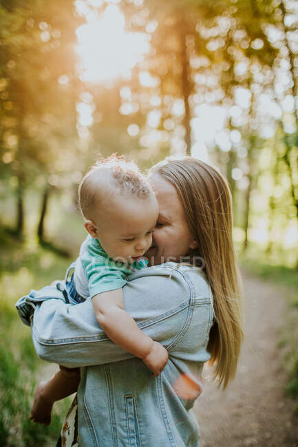 Vertical of happy mother snuggling baby boy outside in forest — Stock Photo