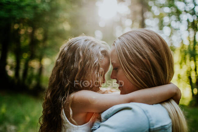 Мама и маленькая дочь обнимаются, улыбаясь на солнце. — стоковое фото