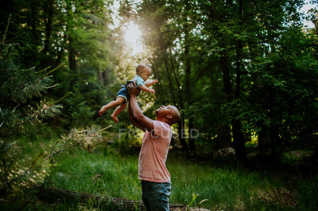 Papà regge il figlio neonato in aria nel bel mezzo della foresta — Foto stock