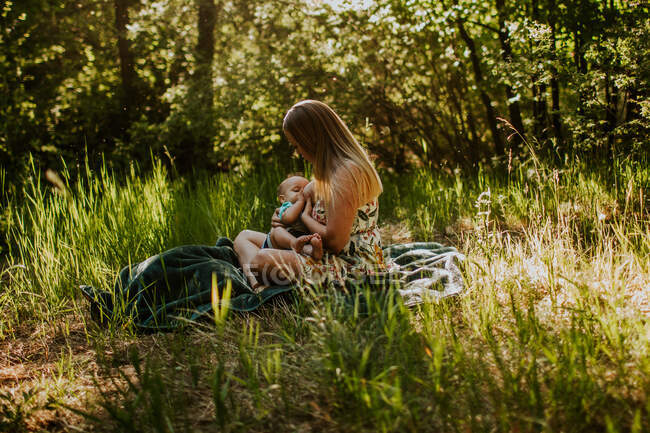 Mother sitting and nursing baby in tall grass — Stock Photo
