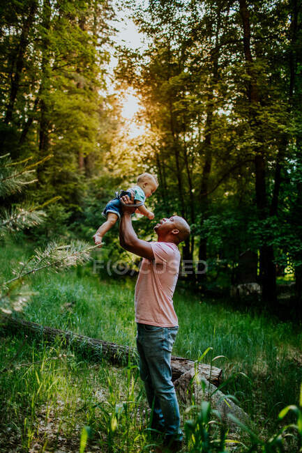 Vertical portrait of dad holding infant son up in the air — Stock Photo