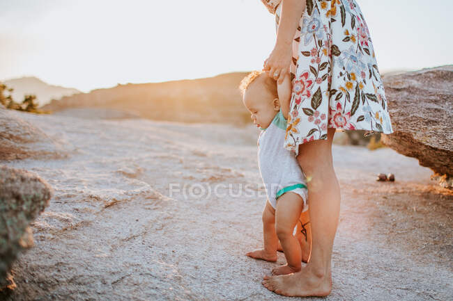 Mom helping baby boy walk on rocks at sunset — Stock Photo